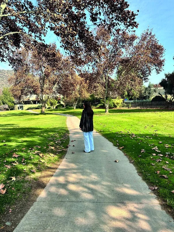 Una mujer de espaldas en un camino de parque, vista desde la cámara del celular